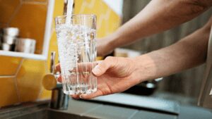 Personne remplissant un verre avec de l'eau du robinet, illustrant une étude de la qualité de l'eau domestique